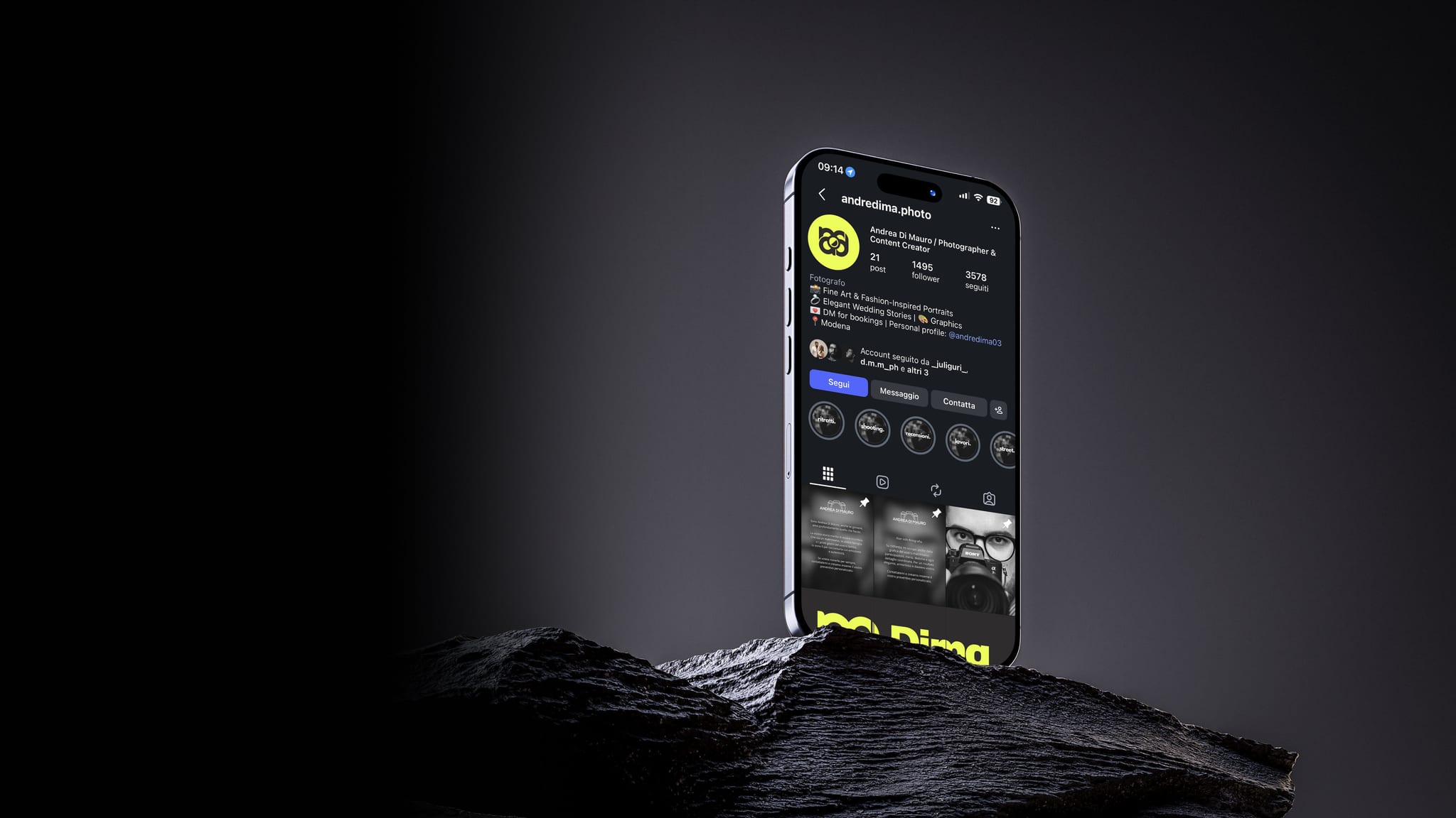 Un telefono in piedi su una roccia scura, contro un fondo grigio: sullo schermo il profilo Instagram di Dima photos, col monogramma nero su giallo fluo, e in fondo il logo in giallo.