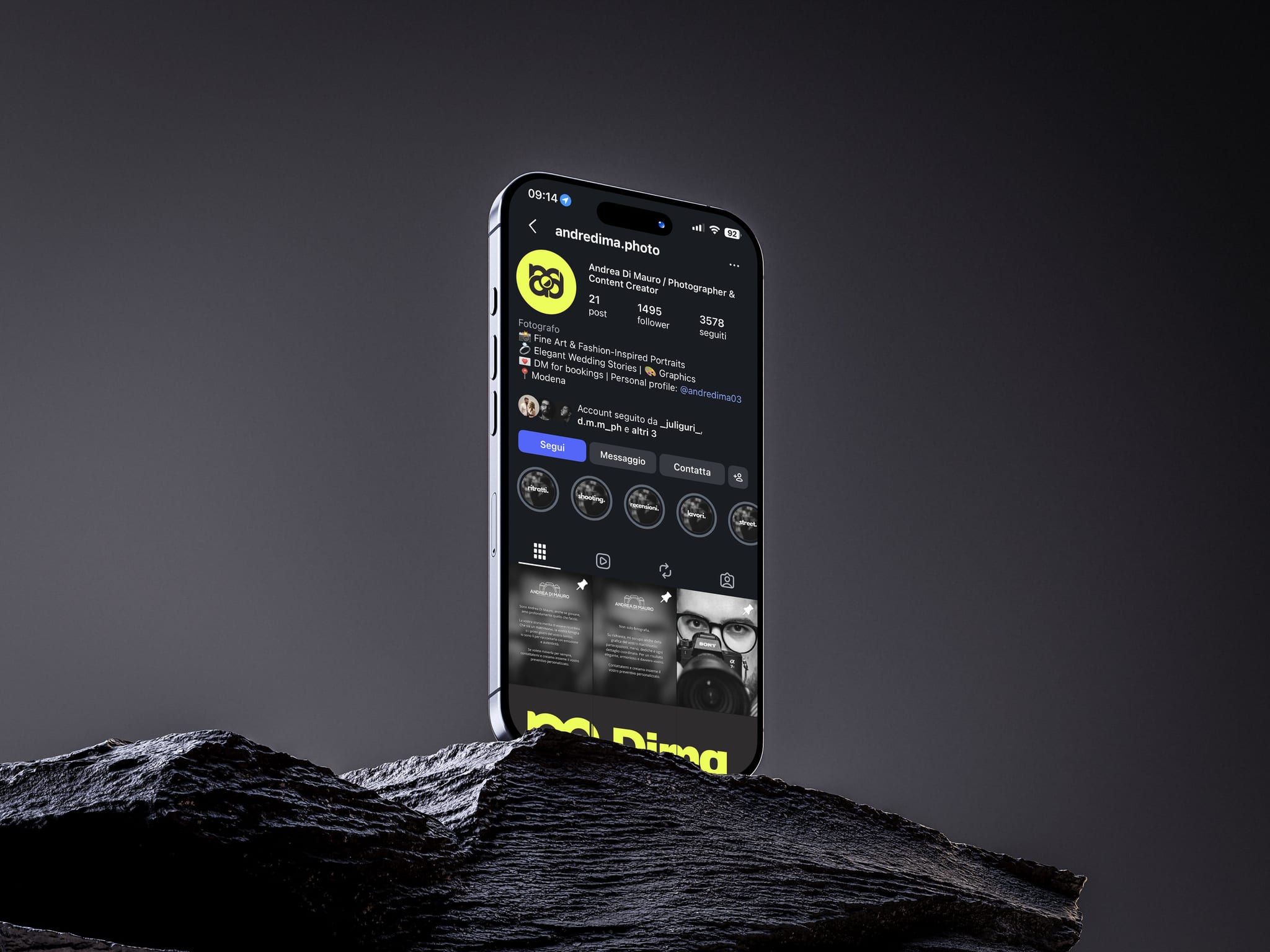 Un telefono in piedi su una roccia scura, contro un fondo grigio: sullo schermo il profilo Instagram di Dima photos, col monogramma nero su giallo fluo, e in fondo il logo in giallo.