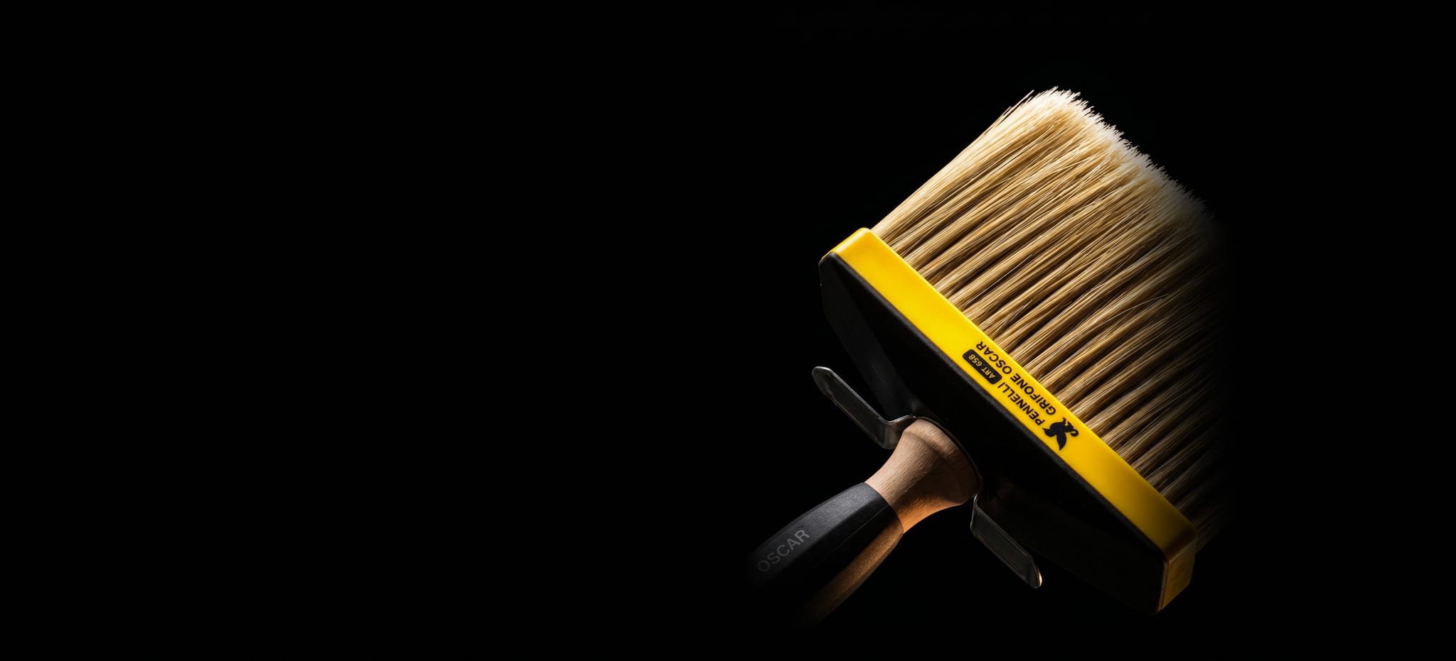 Il plafone 658 di Pennelli Grifone Oscar in diagonale su fondo nero, illuminato al centro: le setole chiare, la montatura gialla col grifone e la scritta «PENNELLI GRIFONE OSCAR», e il manico che si perde nel buio.